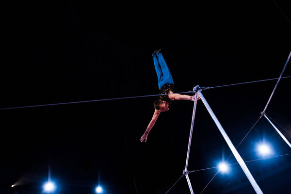 low angle view of athletic man performing on horizontal bars in arena of circus  