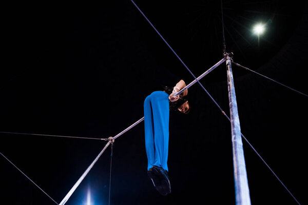 low angle view of flexible gymnast performing on horizontal bars in arena of circus  