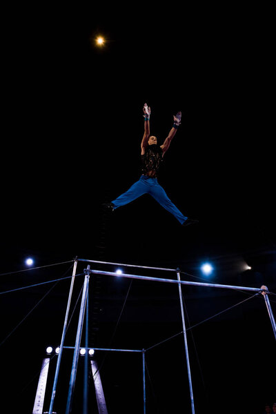 low angle view of gymnast jumping near horizontal bars in arena of circus  