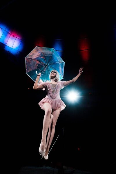 low angle view of happy aerial acrobat in costume holding umbrella and standing on rope 