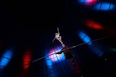 low angle view of handsome gymnast supporting attractive acrobat while holding pole  clipart