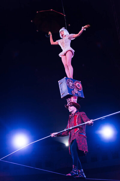 low angle view of man holding pole and supporting attractive acrobat while walking on rope 