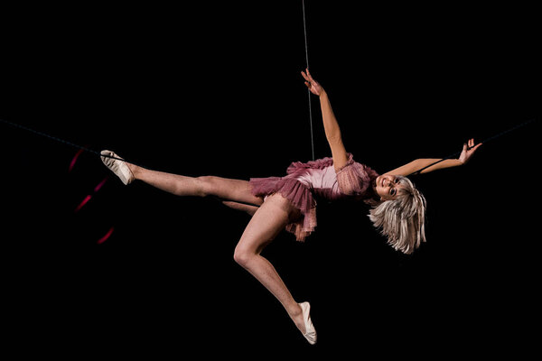 artistic aerial acrobat holding ropes and performing in circus 