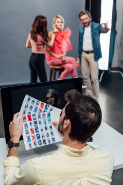Sanat yönetmeninin bilgisayar ekranının yanında fotoğraf kolajı tutarken seçici odak noktası