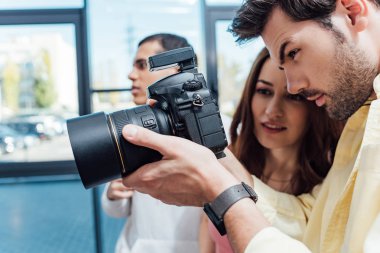 selective focus of attractive art director looking at digital camera near photographer  clipart