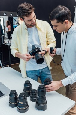 Yakışıklı sanat yönetmeni fotoğrafçının yanında duruyor ve elinde fotoğraf lensi var. 