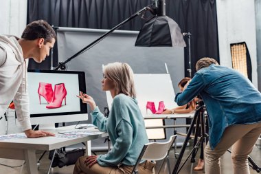 Çekici sanat yönetmeni, bilgisayar monitörünün yanında ayakkabı fotoğrafıyla el kol hareketi yapıyor. 