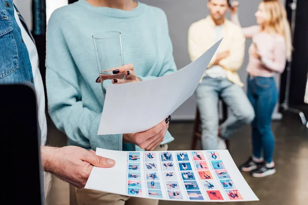 cropped view of art director holding photo collage near assistant with glass of water