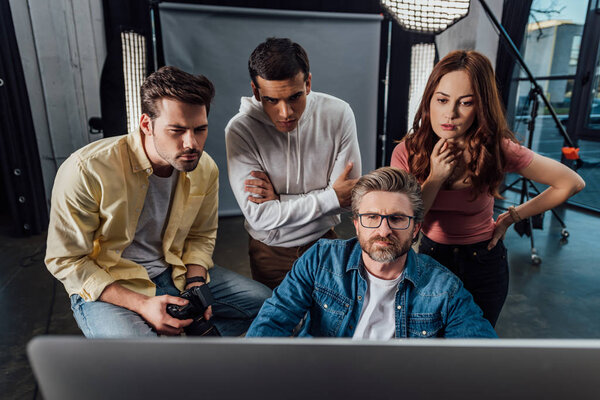 selective focus of creative director and assistants looking at computer monitor in photo studio 