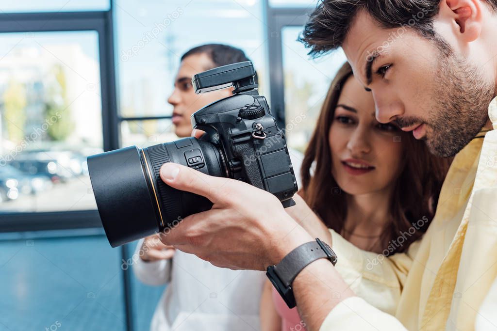 selective focus of attractive art director looking at digital camera near photographer 