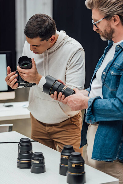bearded art director holding photo lens near photographer 