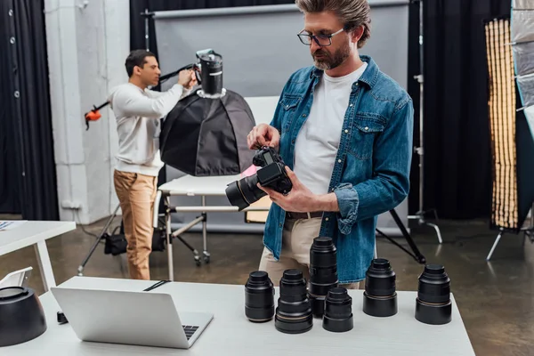 Bebaarde Fotograaf Houdt Digitale Camera Buurt Laptop Tafel — Stockfoto