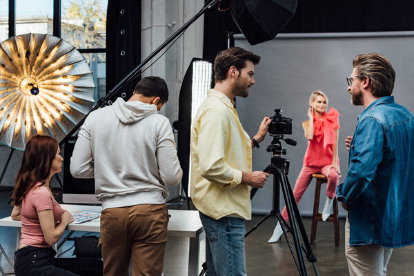 selective focus of art director in glasses looking at photographer near assistants and model 