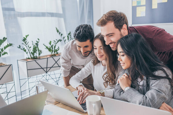 happy multicultural businessmen and businesswomen looking at laptop in office 