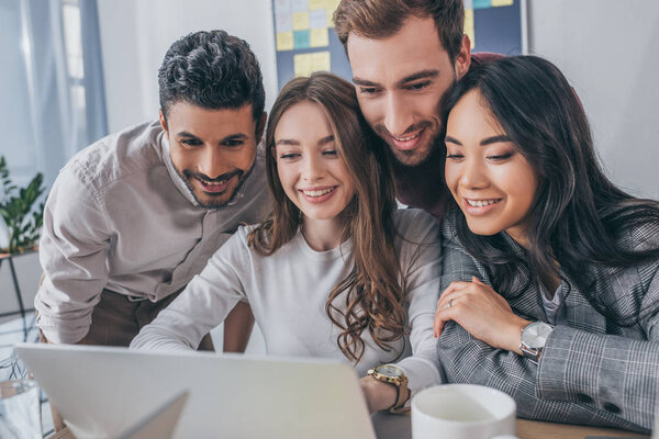 smiling multicultural businessmen and businesswomen looking at laptop in office 