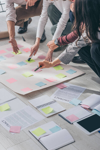 cropped view of scrum masters pointing with fingers at floor with sticky notes near documents 