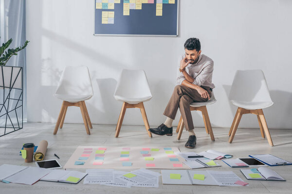 pensive mixed race businessman sitting on chair near sticky notes 