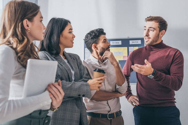 selective focus of handsome scrum master gesturing near multicultural coworkers 