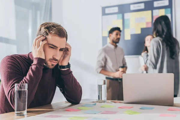 Selective focus of tired businessman with headache near coworkers — Stock Image Selective Focus Tired Businessman Headache Coworkers Royalty Free Stock Photos