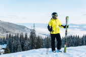 veselý lyžař v helmě drží lyžařské hole a stojí na sněhu proti modré obloze