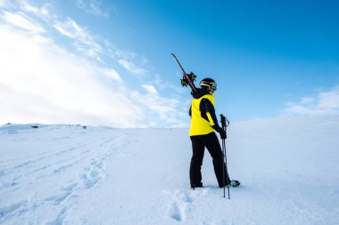 sportsman in helmet standing with ski sticks on slope in wintertime clipart