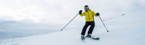 panoramic shot of man in helmet and goggles skiing on slope in wintertime