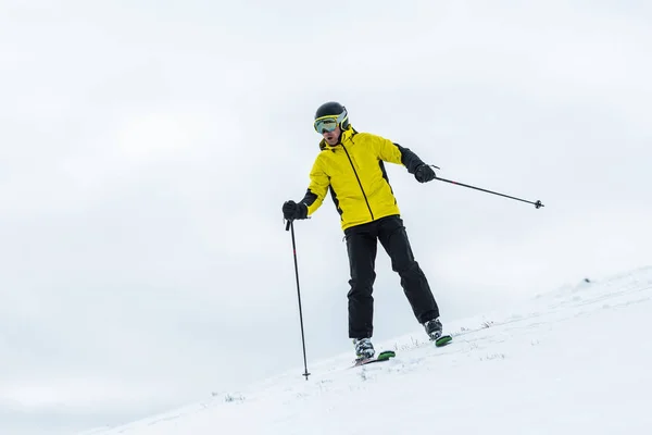 skier in helmet holding ski sticks and skiing on slope in wintertime