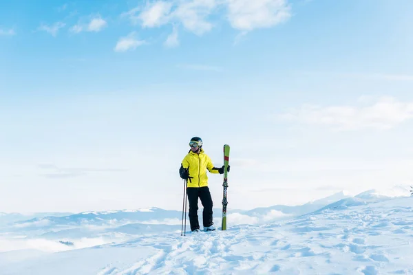 skier in helmet holding ski sticks and standing on snow against blue sky