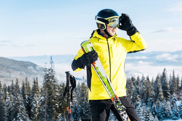 skier touching goggles and holding ski sticks against blue sky