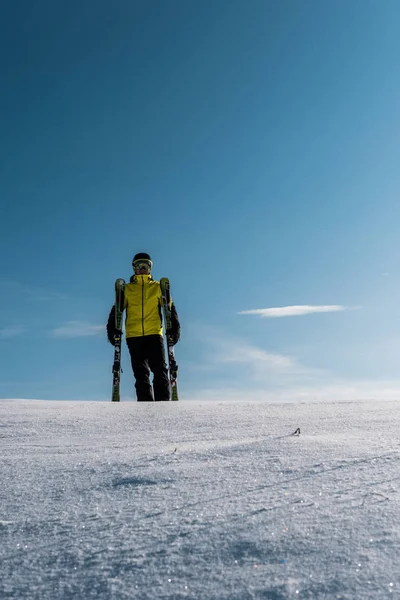 Esquiador con gafas y casco sosteniendo bastones de esquí contra el cielo azul con nubes — Foto de Stock