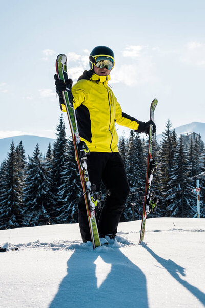 skier holding skis and standing against blue sky in mountains