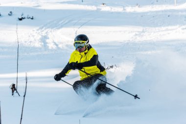 skier in helmet holding ski sticks while skiing on white slope outside clipart