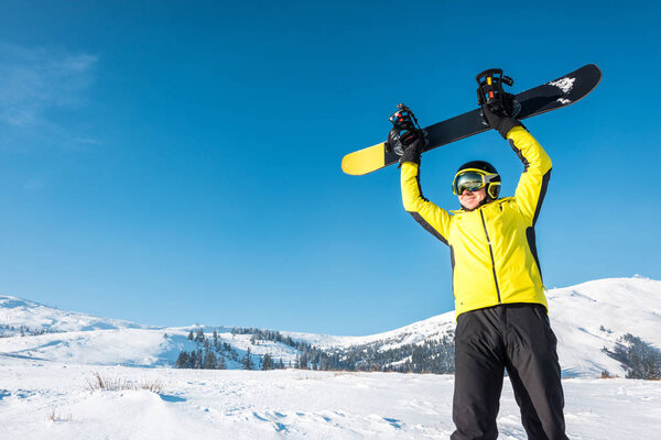 happy sportsman in helmet holding snowboard above head