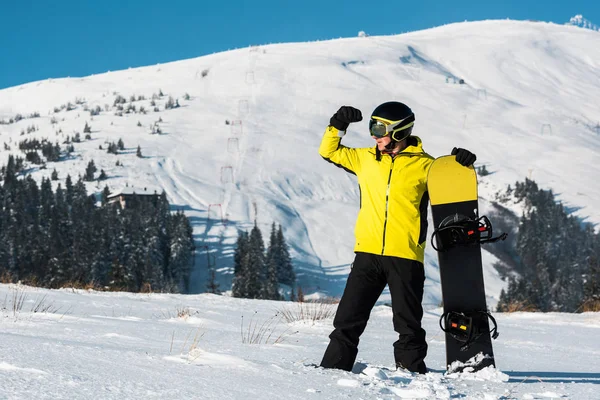 Snowboardos áll a hegyekben, és gesztikulál, miközben félrenéz — Stock Fotó