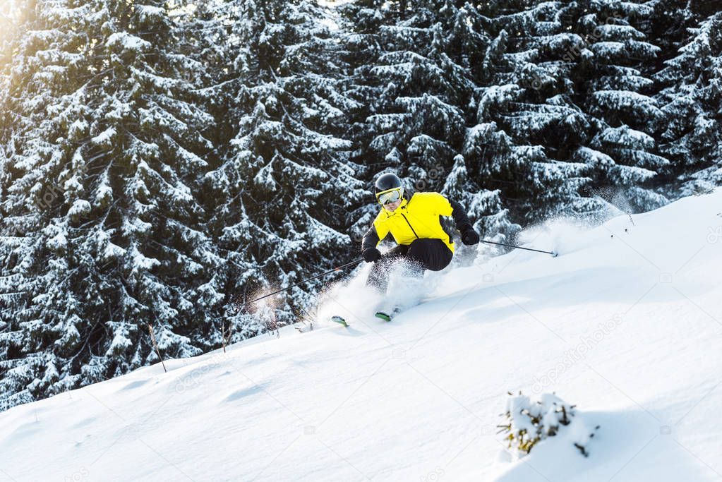 sportsman in goggles holding ski sticks while falling near firs