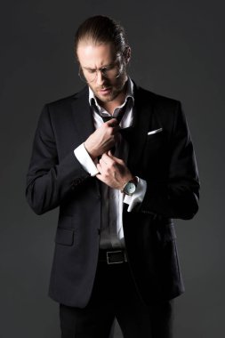 Takım elbiseli yakışıklı adam kravatını gri renkte düzeltiyor.