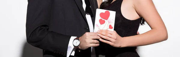 白のパノラマショットでバレンタインデーカードを持っている若いカップルのクロップドビュー — ストック写真