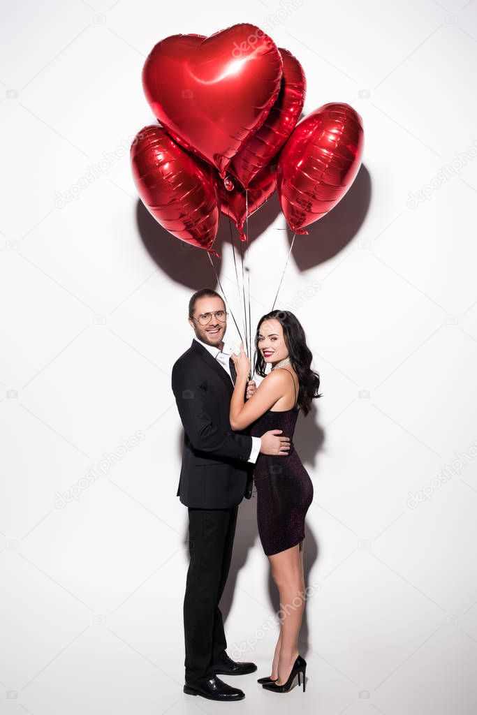 smiling couple holding red heart shaped balloons on valentines day on white