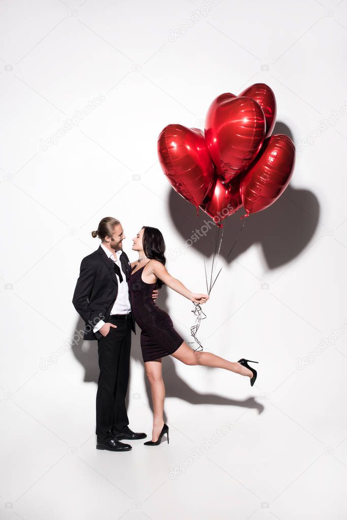 smiling couple holding red heart shaped balloons on valentines day on white