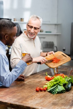 Afro-Amerikan adam elinde bira ve arkadaşı salataya kirazlı domates ekliyor. 