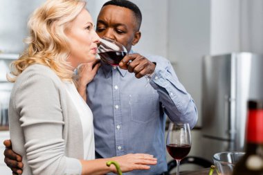 selective focus of african american man giving wine glass to friend in kitchen  clipart