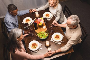 overhead view of multicultural friends holding hands and praying during dinner  clipart