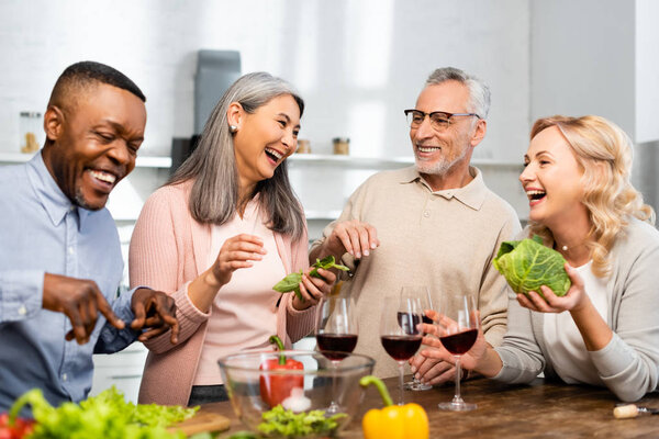 smiling multicultural friends talking and standing near table in kitchen 