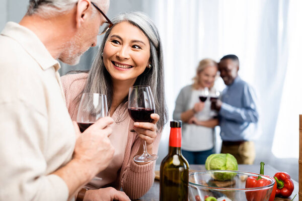 selective focus of smiling multicultural friends talking and holding wine glasses 