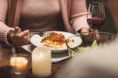abgeschnittene Ansicht einer Frau, die am Tisch sitzt und beim Abendessen Pasta isst 