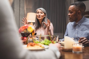 Asain kadın ve Afro-Amerikan erkeğin yemek boyunca arkadaşıyla konuştuğu seçici bir odak noktası. 