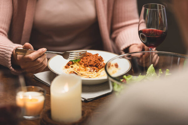 cropped view of woman sitting at table and eating pasta during dinner 