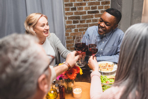 cropped view of woman and man clinking with smiling multicultural friends during dinner 