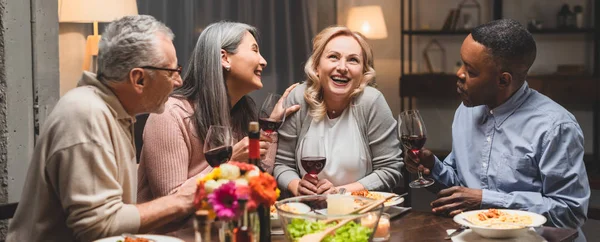 Panoramiczne Ujęcie Uśmiechniętych Wielokulturowych Przyjaciół Mówiących Trzymających Kieliszki Wina Podczas — Zdjęcie stockowe