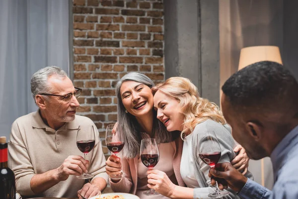 Amigos Multiculturais Sorridentes Abraçando Segurando Copos Vinho Durante Jantar — Fotografia de Stock